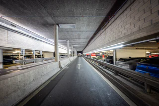 Couloir de circulation du parking couvert P20 Secteur France de Genève Aéroport, avec signalétique directionnelle et espaces de location de véhicules.